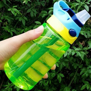 Bottiglia da 480 ml senza perdite con coperchio e cannuccia in verde, giallo e blu davanti a un albero