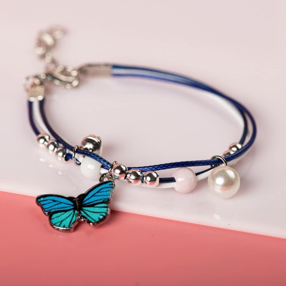 Bracciale con ciondolo a farfalla blu con perle bianche su sfondo bianco e rosa