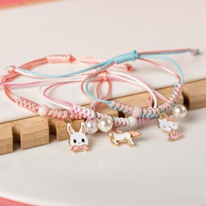 Bracciale intrecciato con ciondolo di perle e animale rosa e blu su sfondo bianco e legno