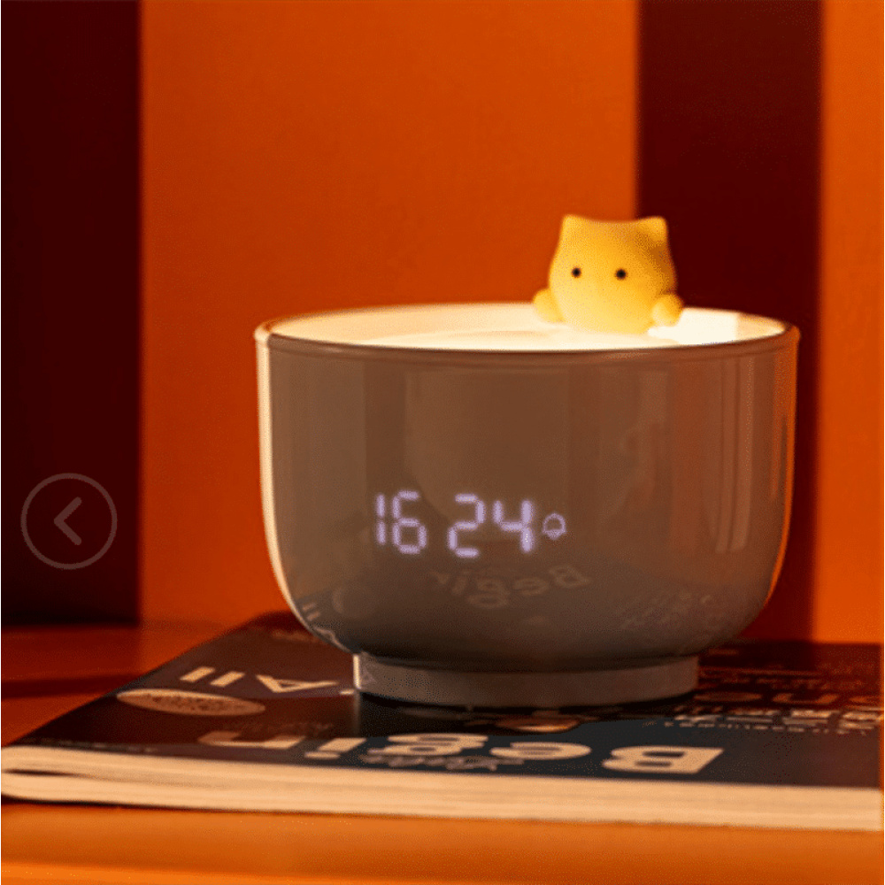 Luce notturna a forma di tazza da tè con sveglia con un gatto su una rivista e uno sfondo arancione