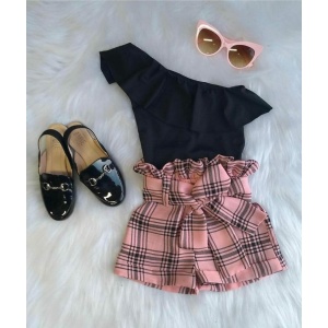 Pantaloncini a quadri rosa con camicia nera, occhiali da sole rosa e scarpe nere lucide su un tappeto bianco