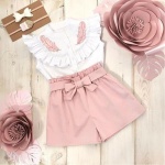 Pantaloncini a tinta unita con una maglietta da ragazza rosa e bianca con piante rosa sul lato e uno sfondo in legno