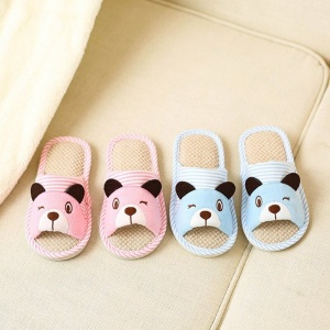 Pantofole a orsetto a righe rosa e blu per bambini su un tappeto beige accanto a un letto