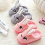 Pantofole con orecchie da coniglio grigie e rosa su tappeto bianco con occhi neri