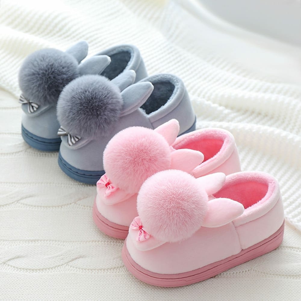 Pantofole a forma di coniglio grigio e rosa su una coperta bianca