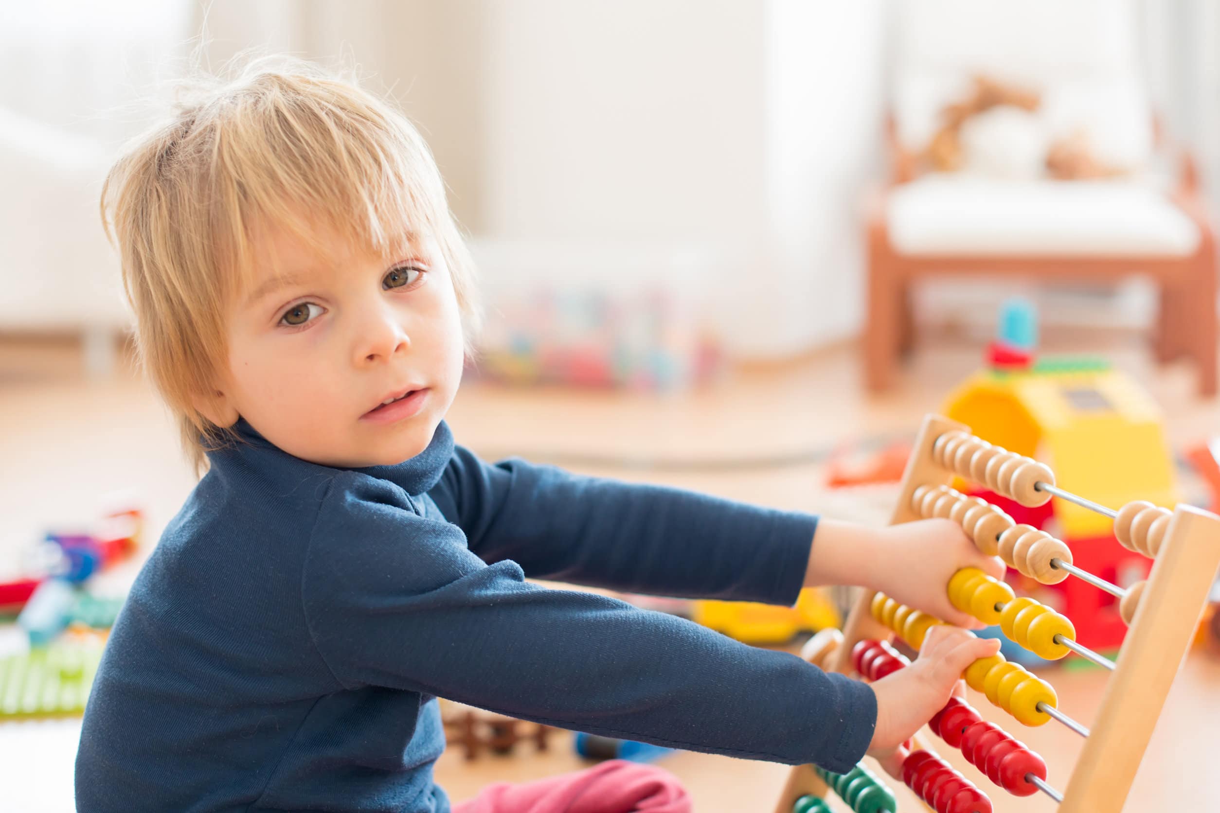 Un bambino con capelli biondi di media lunghezza e un maglione blu che gioca con un abaco colorato per imparare a contare