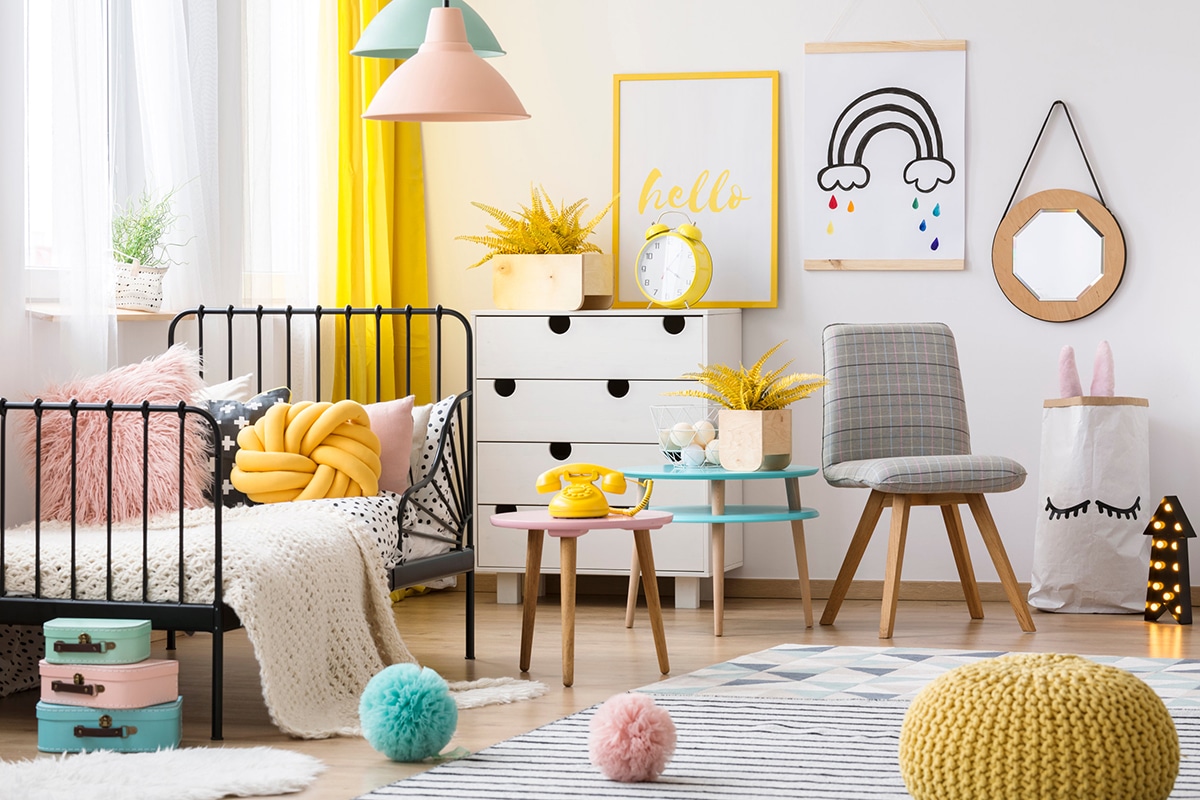Pouf giallo, sedia grigia e lettino all'interno di una colorata cameretta per bambini con poster e decorazioni da parete