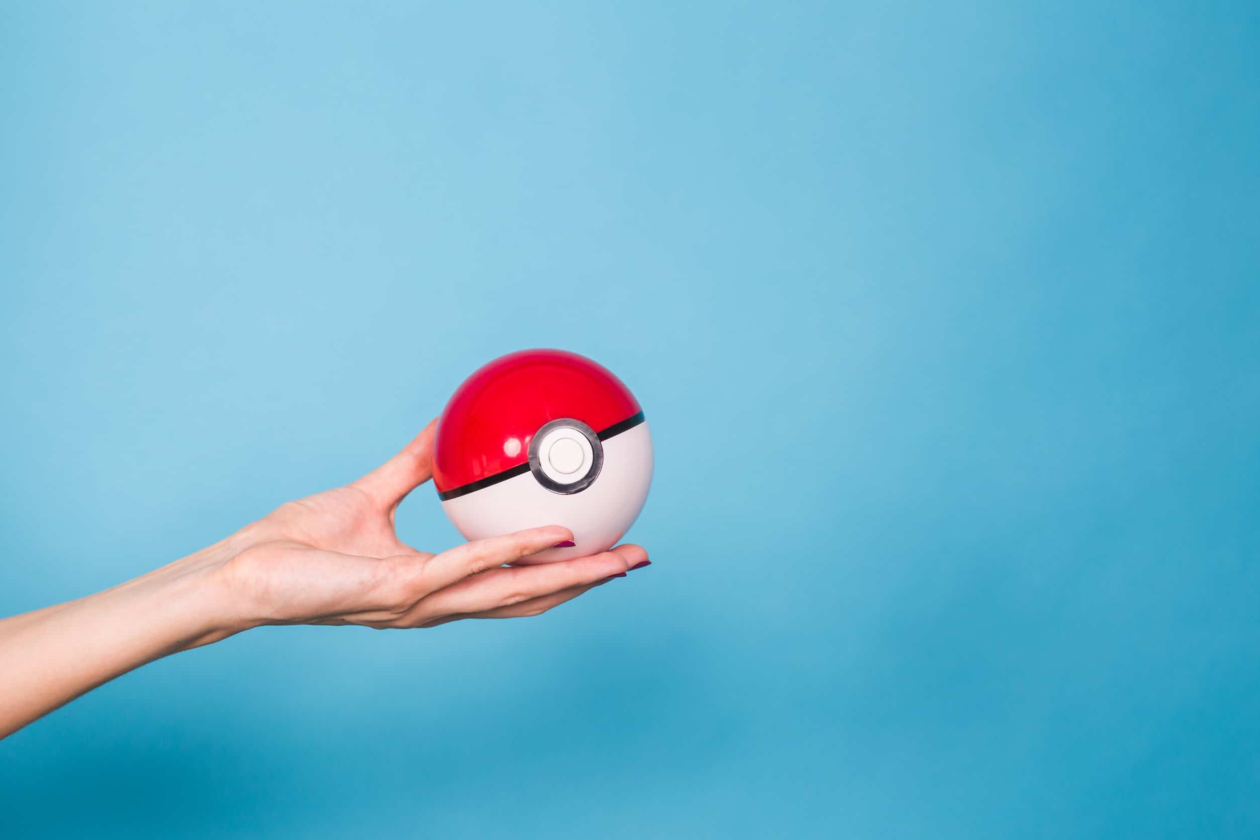Una mano che tiene una pokeball pokémon rossa e bianca su uno sfondo blu
