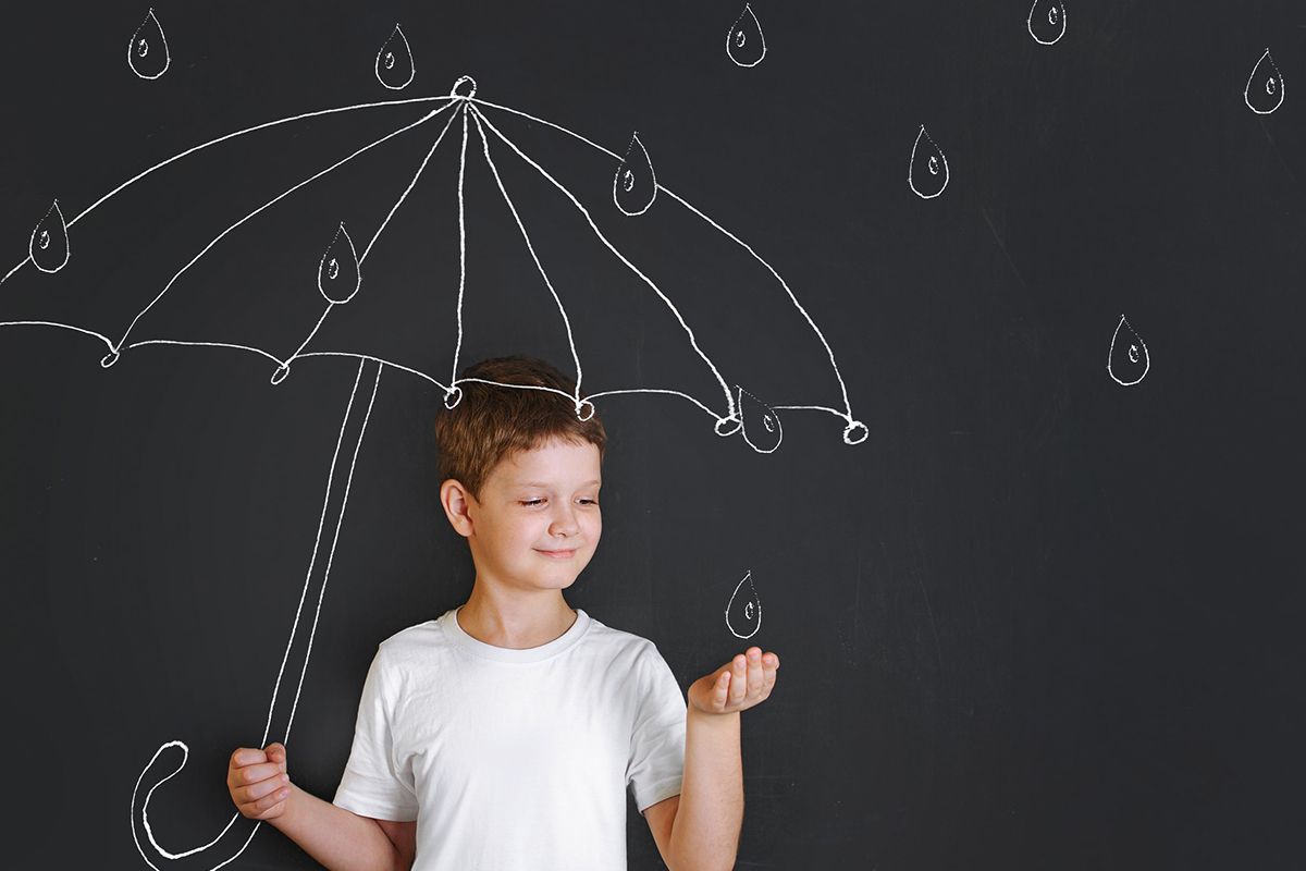 Un ragazzo con una maglietta bianca in piedi davanti a un dipinto che mostra l'ombrello di un bambino e le gocce di pioggia