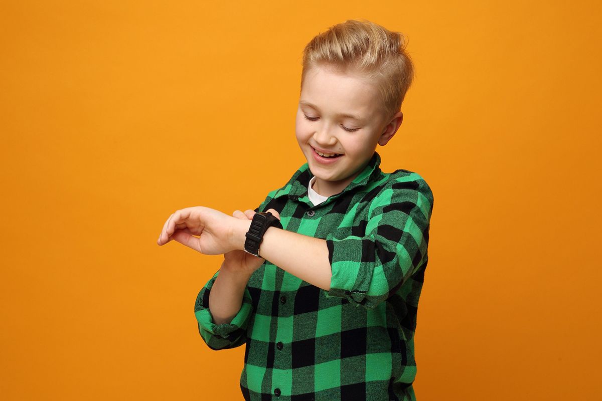 Un giovane ragazzo biondo che indossa una camicia a quadri verde e un orologio da bambino
