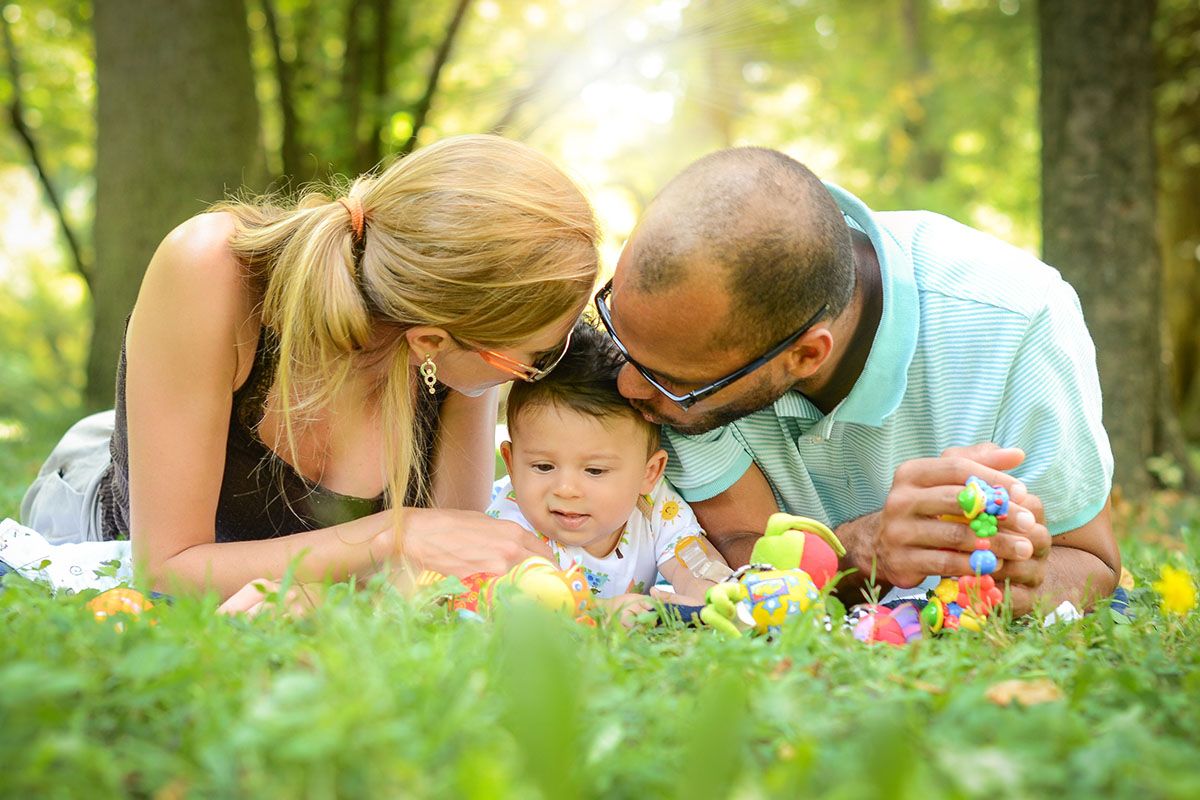 Una famiglia felice sdraiata sull'erba. Al centro ci sono la mamma, il papร e il loro bambino.