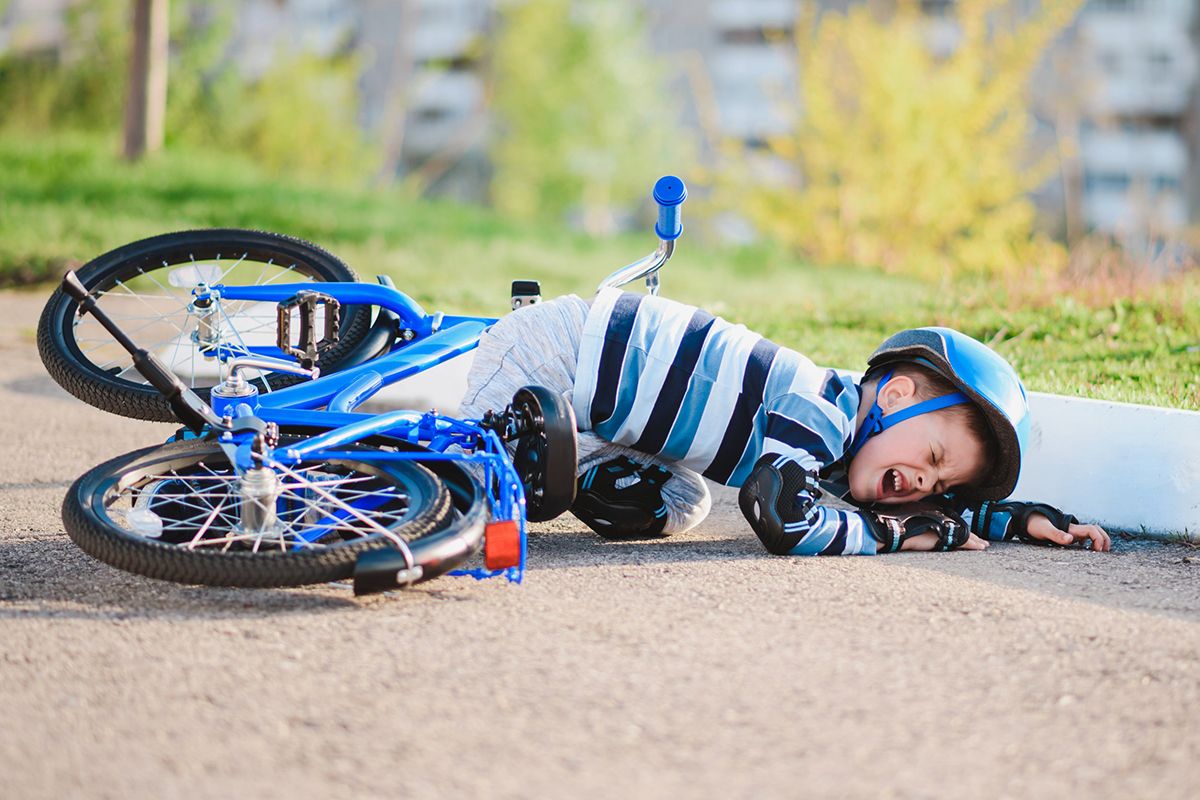 Un bambino รจ morto a causa della sua bicicletta blu. Rimane a piedi e indossa un casco da bicicletta, protezioni per la ginocchia e guanti protettivi neri