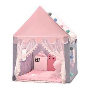 Un teepee per bambini a forma di casetta rosa, con la parte anteriore aperta e due tende appese ai lati. Ai lati ci sono delle piccole finestre. All'interno, c'è un pavimento imbottito rosa e cuscini rosa.