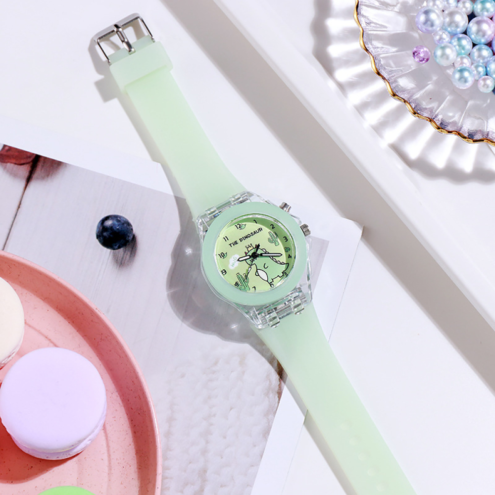 Un orologio verde con un piccolo dinosauro su un tavolo bianco.