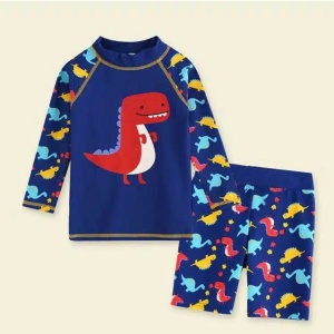 un set di costumi da bagno per bambini, pantaloncini e una maglietta blu con un motivo di dinosauri su sfondo beige