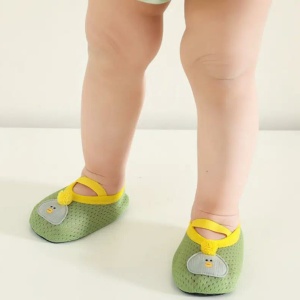 un bambino è in piedi, con le sole gambe visibili, e indossa piccole scarpine verdi, morbide e traspiranti