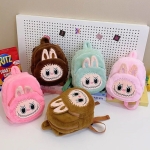 Diversi zainetti in peluche morbido con faccia di mostriciattolo Labubu, orecchie da coniglio e spallacci abbinati, su una scrivania. 5 varianti di colore.