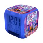 Sveglia K-pop Demon Hunters funzione luce notturna di colore blu con un display digitale. Sulle altre facce, decorazioni con i personaggi del film e il nome in maiuscolo. Su sfondo bianco.